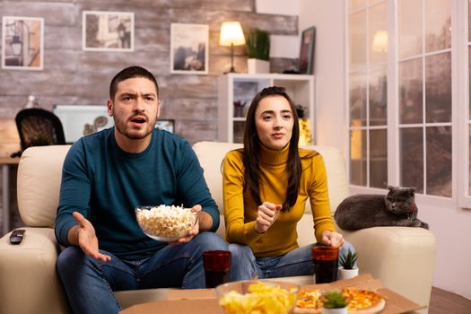 Couple cheering for their favourite team while watching TV and eating fast food