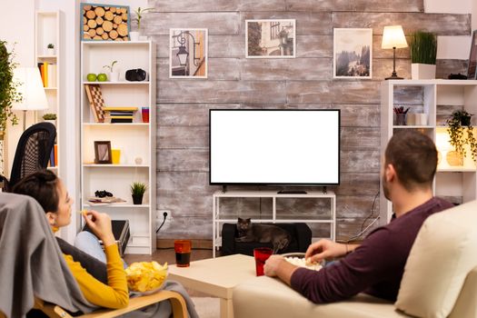 Couple looking at isolated TV screen in cozy living room while eating takeaway food