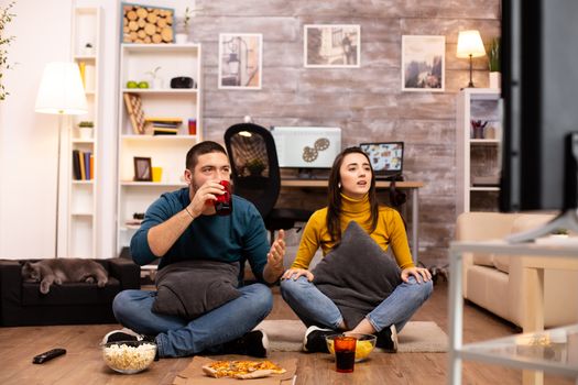 Couple sitting on the floor and watching TV in their living room.