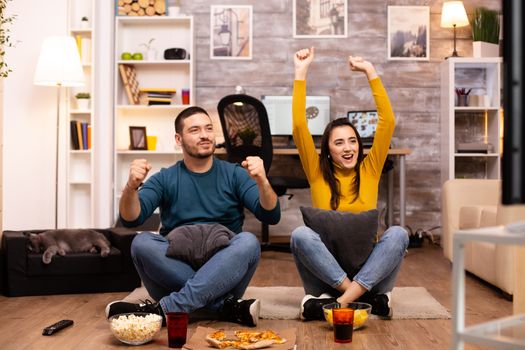 Couple sitting on the floor and watching TV in their living room.