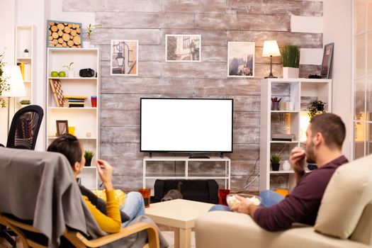 Couple looking at isolated TV screen in cozy living room while eating takeaway food