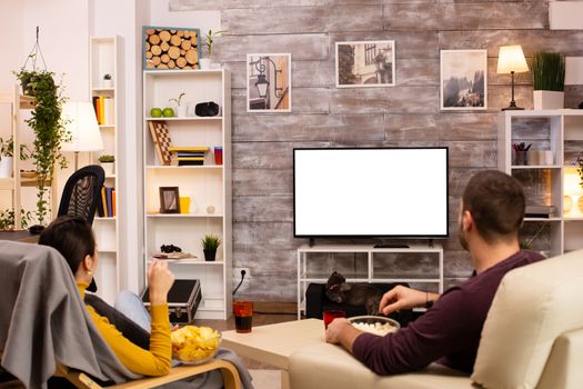 Couple looking at isolated TV screen in cozy living room while eating takeaway food