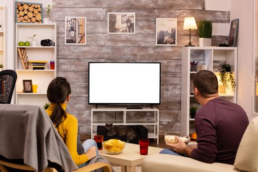 Couple looking at isolated TV screen in cozy living room while eating takeaway food