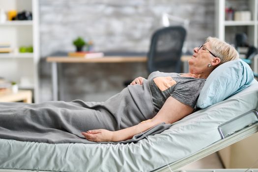 Old granny sleeping in a modern nursing home room. Retired woman.