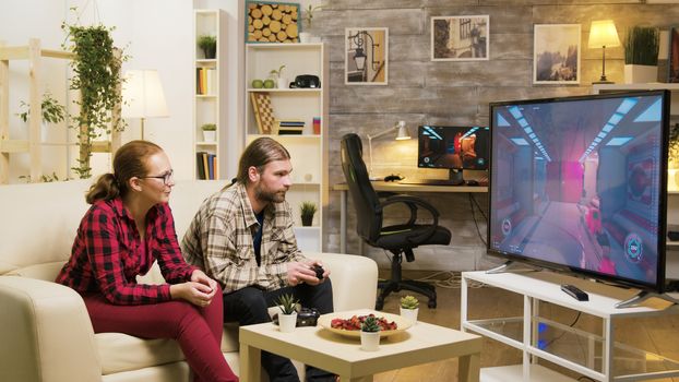Cheerful girlfriend talking with her boyfriend while he's playing video games on tv using wireless joystick.