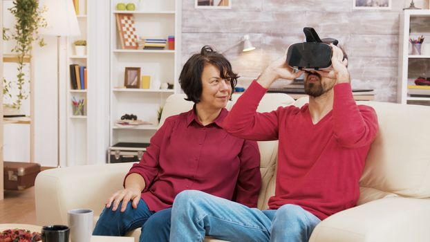 Nephew showing his grandmother how to use VR goggles in living room.