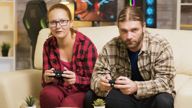 Focused couple playing online video games sitting on couch in living room. Playing games using wireless controllers.
