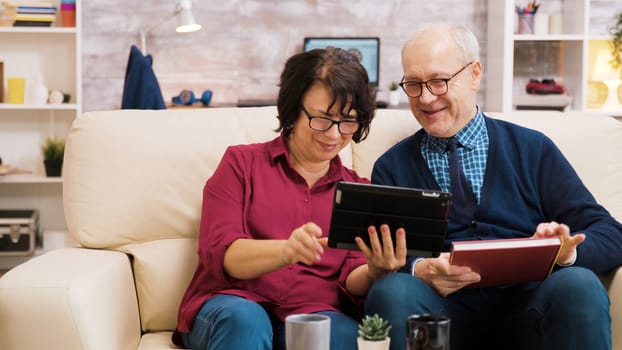 Senior couple waving at tablet during a video call. Elderly people sitting on sofa.
