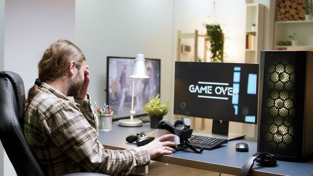 Man sitting on gaming chair taking off his vr headset. Game over for male gamer with long hair.