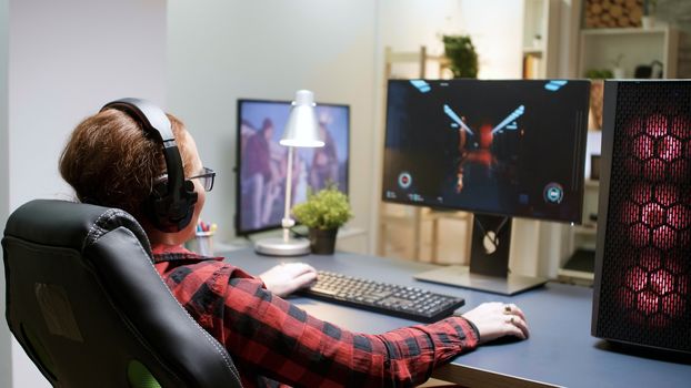 Side view of young female playing shooter games sitting on gaming chair. Powerful computer rig with neon spinning fans