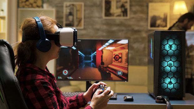 Professional female gamer using vr headset and wireless controller to play computer games. Man texting on phone in the background.