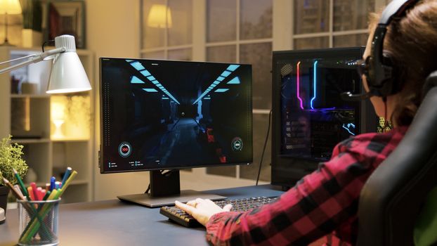 Female gamer with headphones playing shooter games on computer and talking with others players.