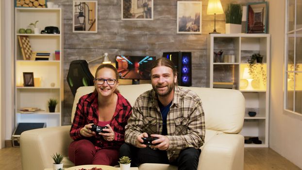 Young couple jumping up from the couch celebrating their victory while playing video games using wireless controllers.