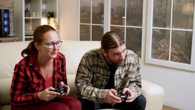 Hipster couple sitting on sofa playing video games using wireless controller. Man and woman giving high five.