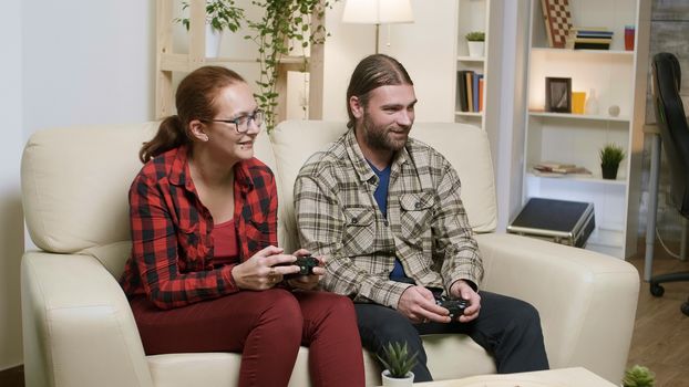 Husband and wife sitting on sofa playing video games using wireless controller.