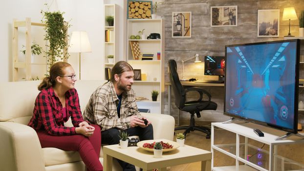 Cheerful girlfriend talking with her boyfriend while he's playing video games on tv using wireless joystick.