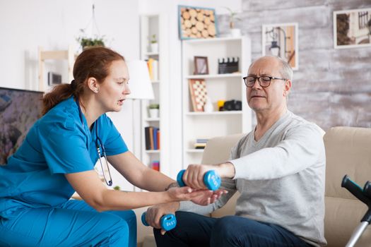 Senior man in nursing home doing physiotherapy with dumbbells with help from nurse.