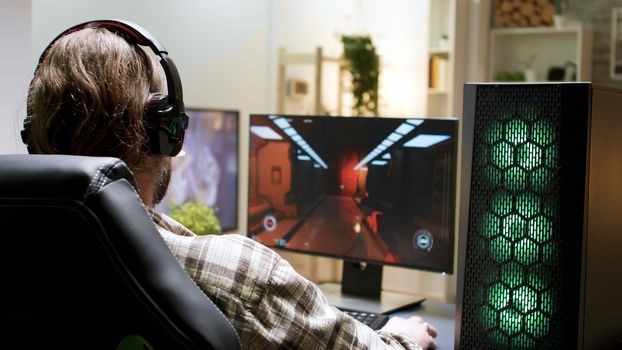 Over shoulder shot of man with long hair playing shooter games sitting on gaming chair.