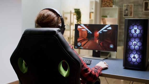 Back view of woman with red hair playing online shooter games sitting on gaming chair.