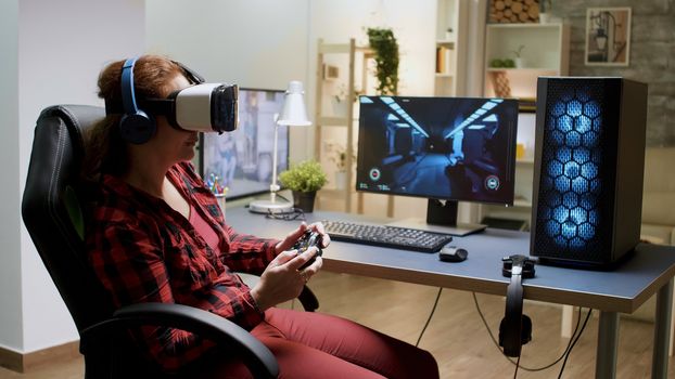 Side view of woman with red hair wearing vr goggles while playing video games with wireless controller.