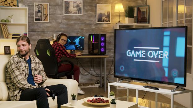 Game over for a young playing video games with vr headset sitting on sofa. Girlfriend looking at boyfriend after losing at video games.