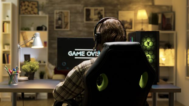 Over shoulder shot of man after losing at video games on computer with headphones on. Game over while playing games.