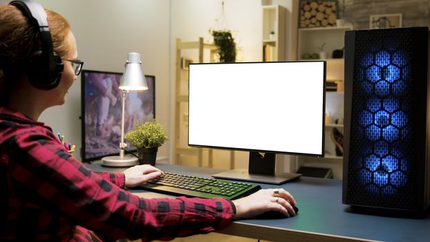 Woman with headphones playing games on green screen computer in living room. Woman sitting on gaming chair.