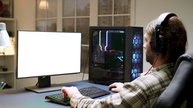 Pro bearded gamer with long hair playing video games on computer with green mock-up.