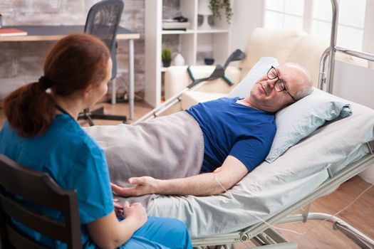 Male pensioner in nursing home talking with female doctor sitting on bed.