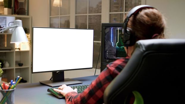 Over shoulder shot of pro female gamer playing on computer with green mock-up screen.
