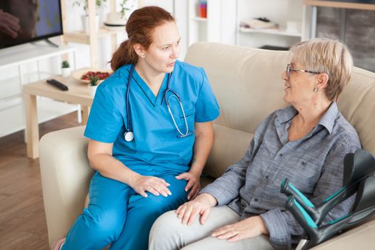 Health visitor with stethoscope on a couch in a nursing home talking with old woman.