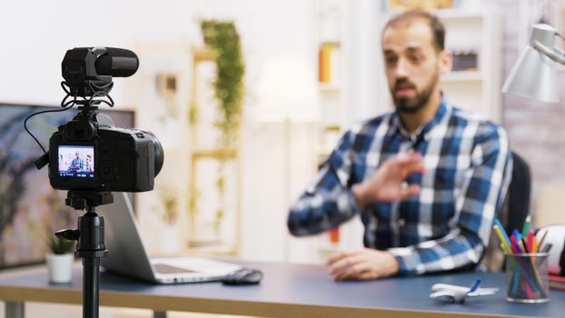 Vlogger sitting at desk in living room talking and looking at the camera. Famous influencer recording for social media.