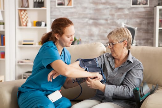 Female nurse using digital blood pressure device on senior woman in nursing home.