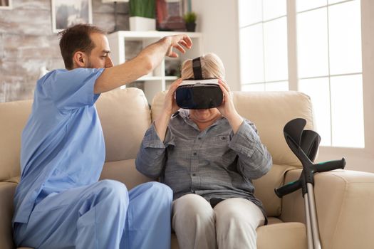 Male doctor in nursing home helping senior woman to use vr headset.