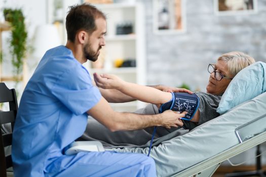 Young doctor in nursing home checking old woman blood pressure using digital device.