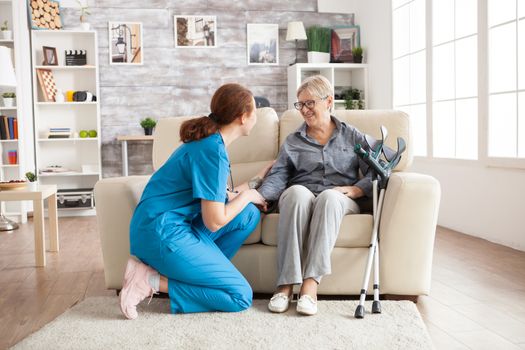 Female nurse talking with an old woman in a nursing home.Old woman on couch with crutches.
