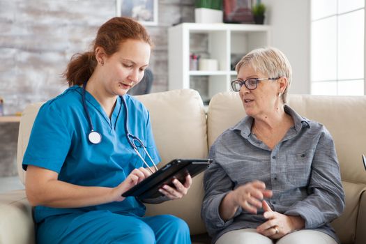 Senior woman and female nurse with tablet sitting on couch in a nursing home.