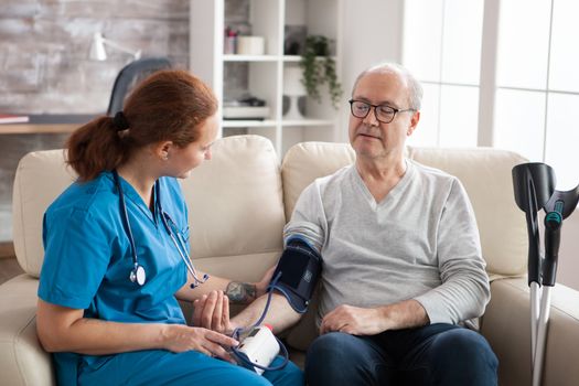 Senior man in nursing home with digital blood pressure device on his arm. Female doctor with old patient.