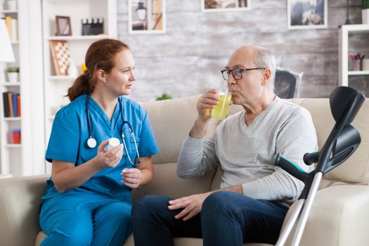 Female nurse with red hair in nursing home giving senior man with crutches pills for his sickness.