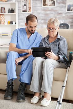 Young doctor reading diagnostic on tablet for senior woman in nursing home.
