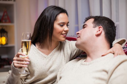 Man looking into her wife eyes sitting on couch celebrating christmas. Woman holding a glass of champagne.