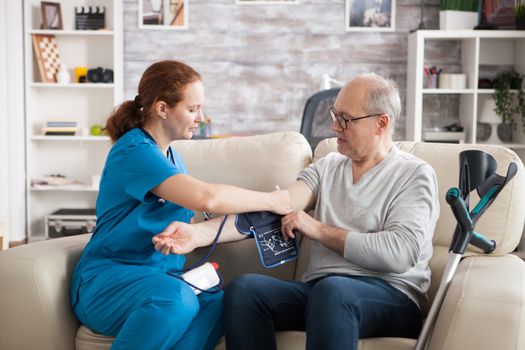 Young doctor in nursing home taking digital blood pressure of old man.
