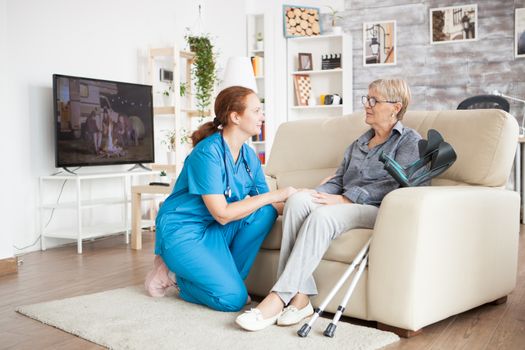 Nurse in knees talking with old woman in a nursing home. Old woman with crutches.