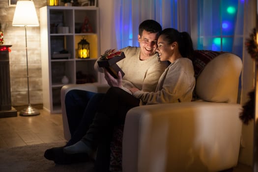 Couple in love on christmas day sitting on couch looking at magical present.