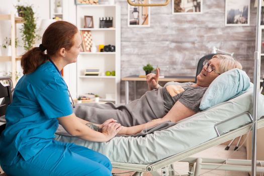 Old woman laying in bed in a nursing home talking with female doctor.