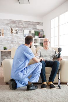 Young doctor holding old man arm in nursing home while talking with him. Happy retirement.