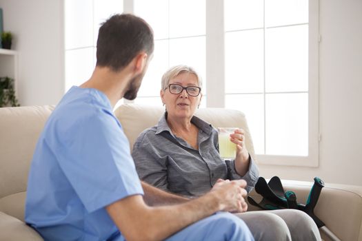 Doctor sitting on couch in nursing home talking with senior woman with crutches while she's taking her pills.