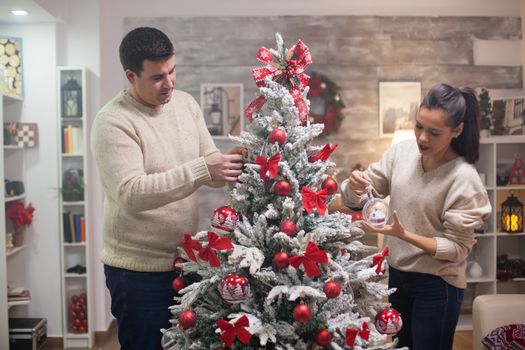 Handsome young man and his girlfriend preparing their christmas tree in living room.