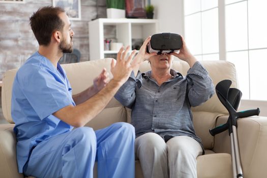 Elderly aged woman using virtual reality glasses in nursing home while doctor explain her disease.