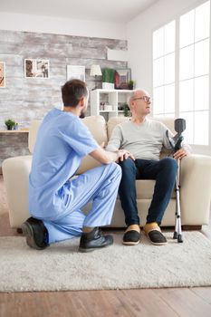 Young doctor in nursing home talking with old man with alzheimer's disease while he's looking lost.